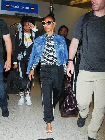 Jada Pinkett Smith’s travel style…blue denim jacket worn over a monochrome spot print shirt, black luxe joggers, white barely there sandals and a pair of white framed sunnies. Celebrity airport outfits | star style fashion - flipped