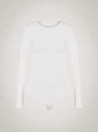 Selena Gomez white long sleeved crew neck bodysuit, Wolford BERLIN BODY. Worn with a selection of silver organic shaped bangles and drop earrings. For the cover of Rolling Stone, December 2022 issue | celebrity photoshoot outfits | star style fashion | minimalist bodysuits