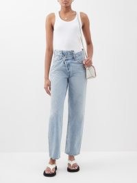 Selena Gomez’ light blue asymmetric wrap waist jeans, AGOLDE Crossover-button straight-leg jean. Worn with a black trench coat, cowl neck blouse and a pair of fluffy mule slippers. On Instagram, Novemeber 2022 | celebrity denim fashion | social media style