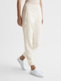 REISS MILLY TECHNICAL JOGGERS CREAM / womens luxe jogging bottoms / women’s sportswear inspired clothes / chic casual sports fashion / cuffed hems / feature utility pocket