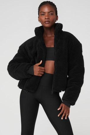 Addison Rae black zip up fleece, alo yoga SHERPA SNOW ANGEL PUFFER. Worn with black shorts, white over the knee socks, a pair of UGG slippers and carrying a small black nylon shoulder back by Prada. Out in Los Angeles, 11 November 2022 | casual celebrity street style | faux shearling fur jackets