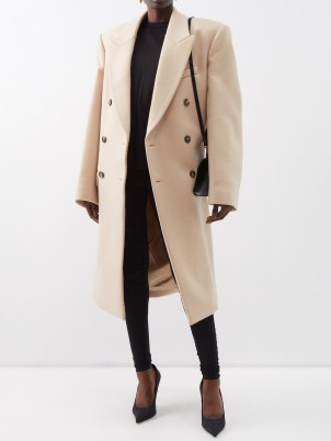 Rosie Huntington-Whiteley’s beige oversized longline coat, WARDROBE.NYC X Hailey Bieber double-breasted wool coat. Worn with a black hoodie and a pair of joggers, white trainers, a baseball cap and carrying a large quilted shopper bag. Out in London, March 2023 | celebrity street style coats | models off duty clothing